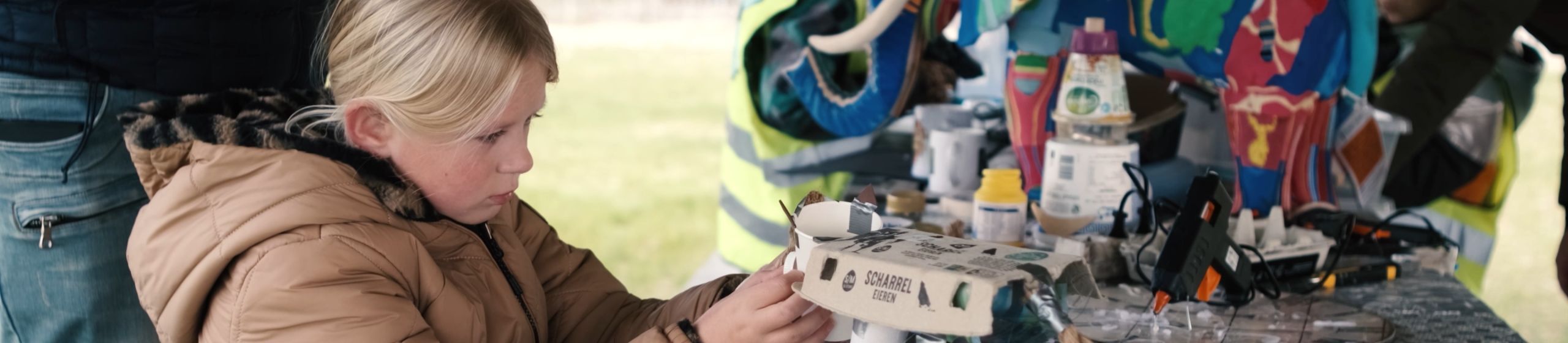 Kind werkt aan tafel met gerecycled materiaal terwijl een geverfde olifant zichtbaar is. 