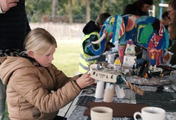 Kind werkt aan tafel met gerecycled materiaal terwijl een geverfde olifant zichtbaar is. 